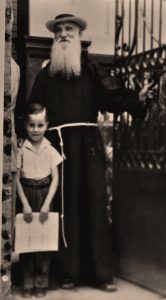 Foto antigua de sacerdote con estudiante frente a portón de casa.